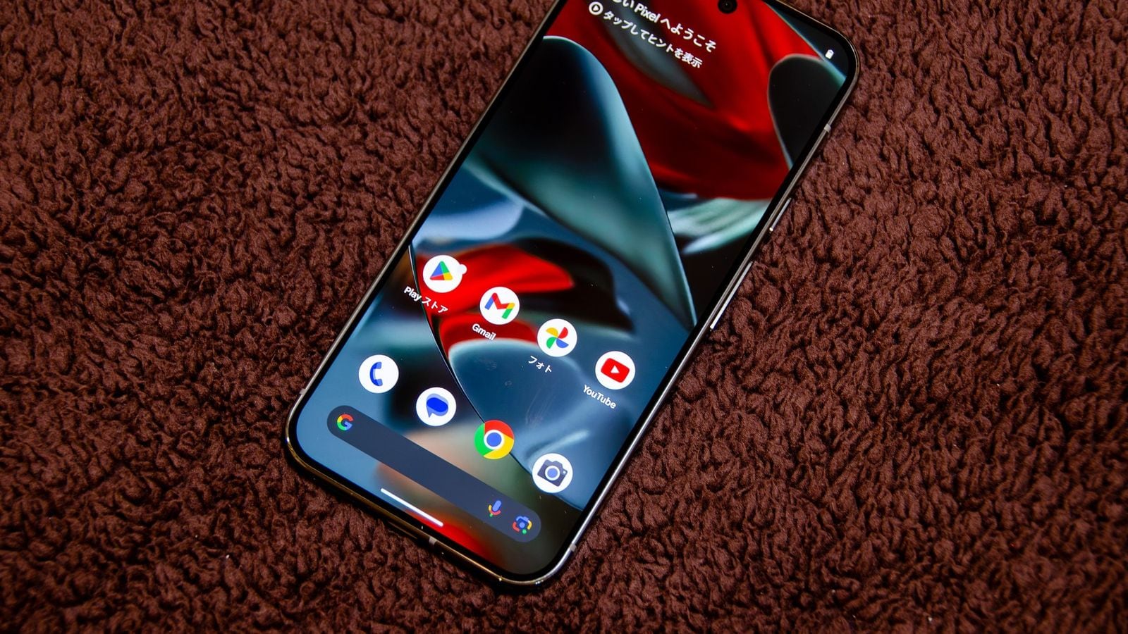 Google Pixel telefón na textilnom podklade so zobrazenou domovskou obrazovkou Androidu a ikonami aplikácií