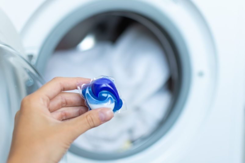 Kapsula na pranie v ruke pred otvorenou práčkou
