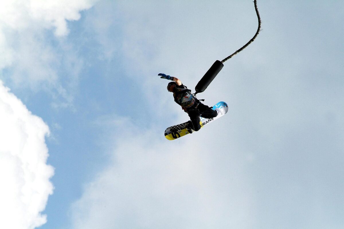 Muž so snowboardom na nohách pri skoku na bungee lane proti oblohe